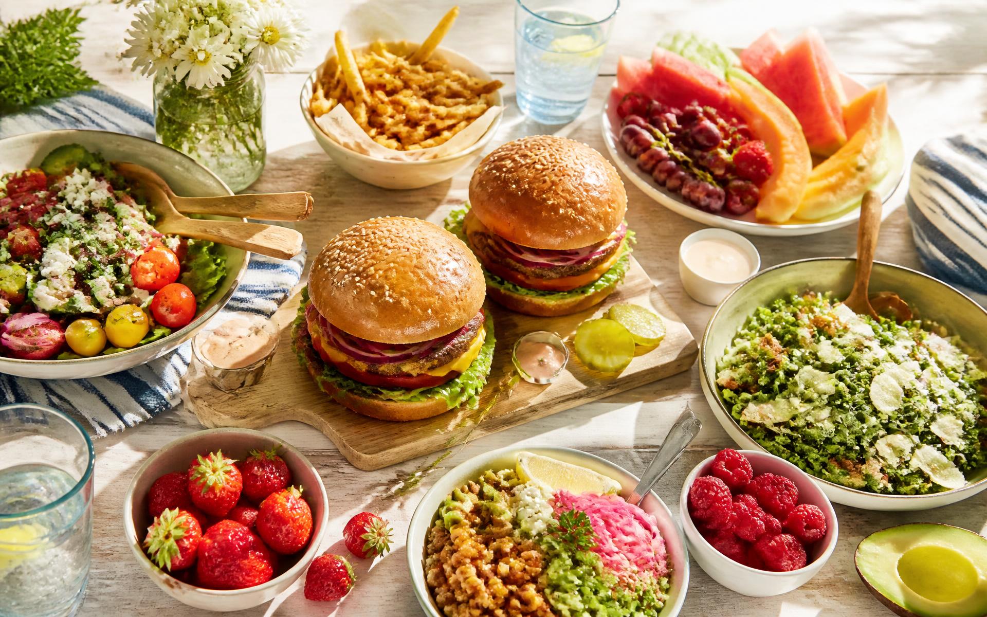 Table full of fresh burgers, salads and fruit in bright sunlight